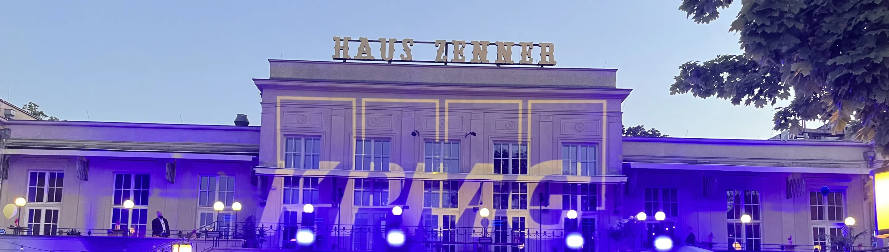 Abendliches Sommerfest vor dem Haus Zenner in Berlin: violette Lichtinszenierung, KPMG-Logoprojektion auf der Fassade und feiernde Gäste