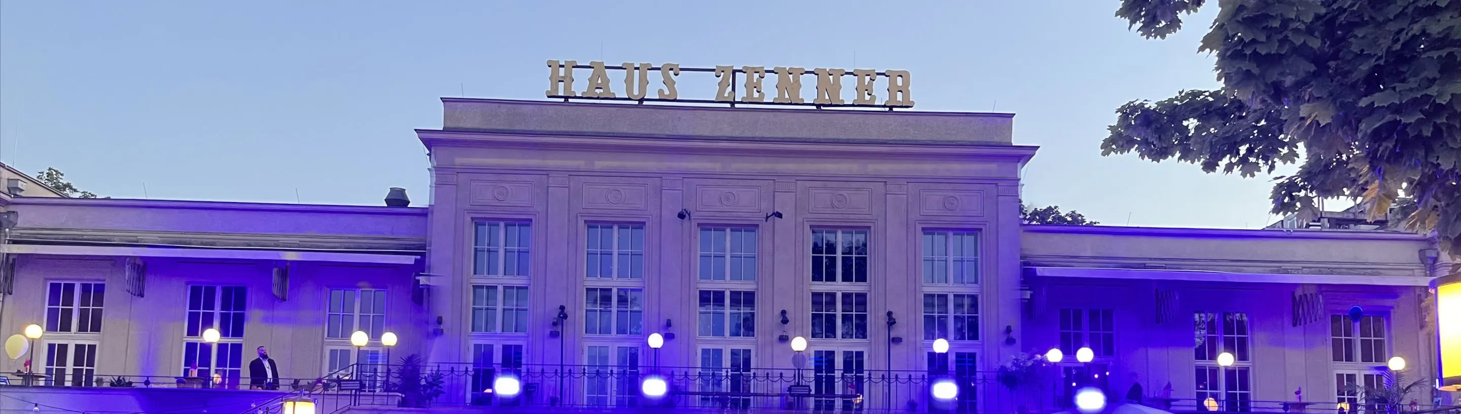 Abendliches Sommerfest vor dem Haus Zenner in Berlin: violette Lichtinszenierung und feiernde Gäste