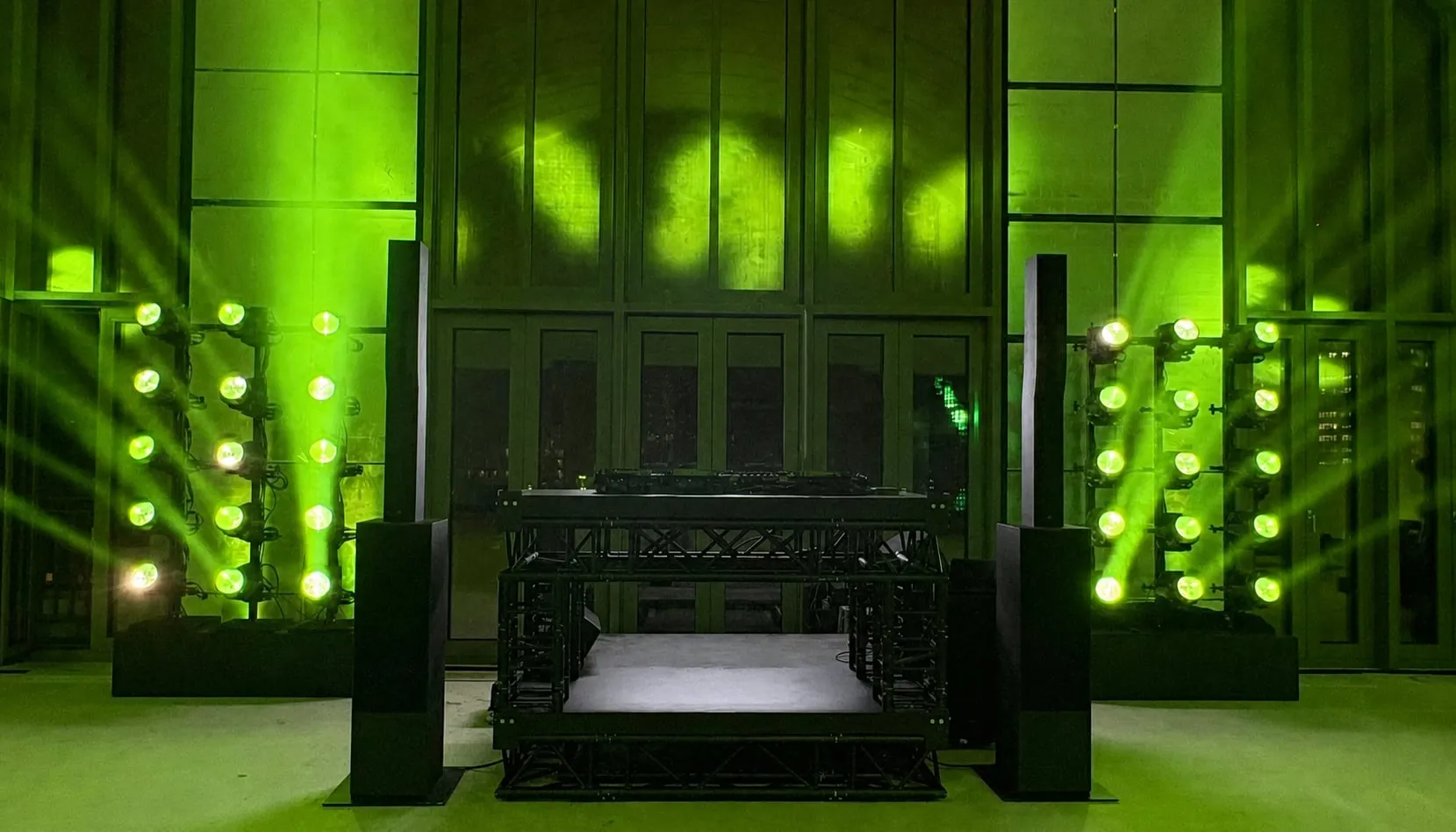 Grün angestrahlte Fassade mit Lichtinstallation über der DJ-Bühne